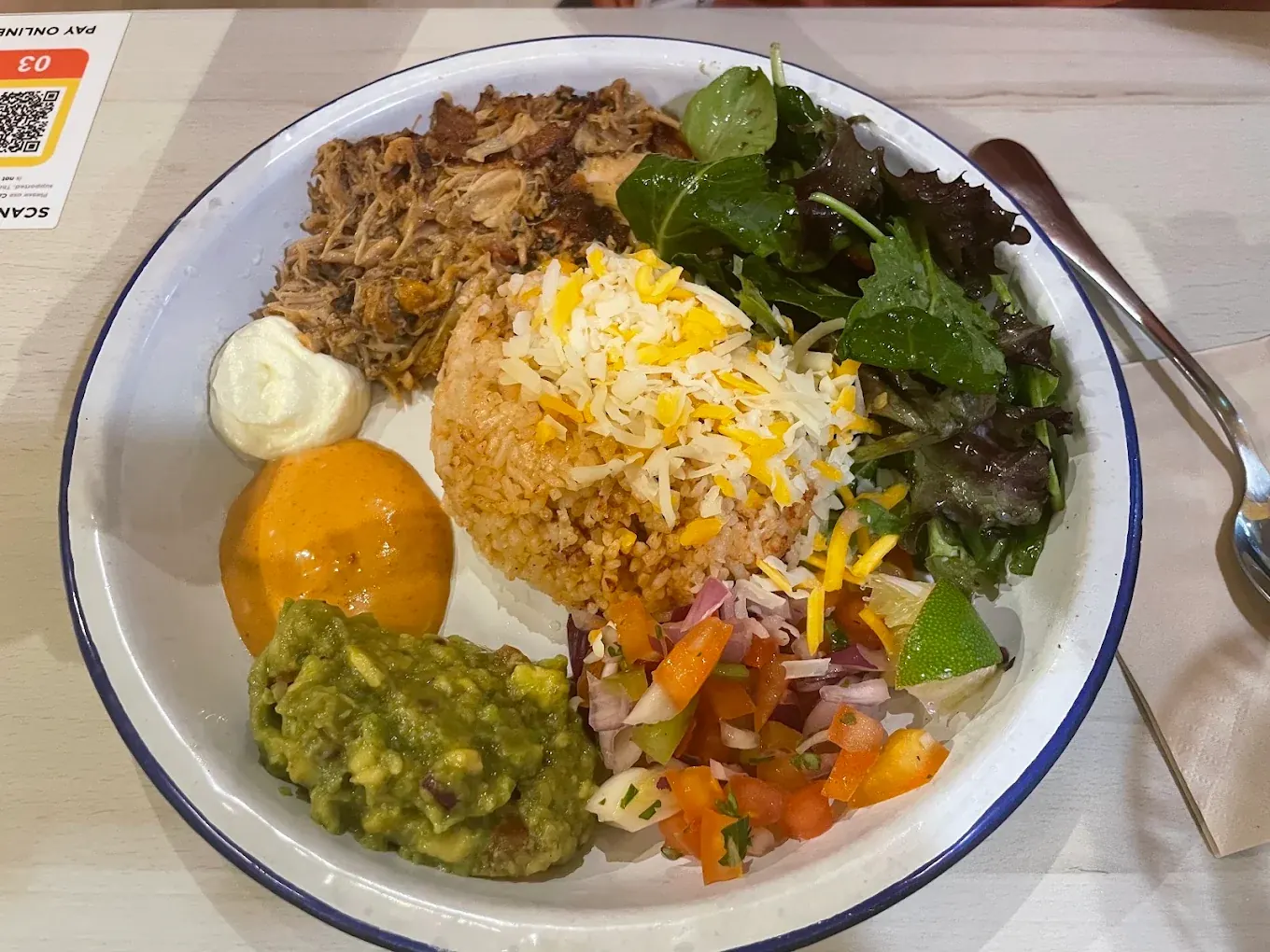 An overhead rice bowl with shredded meat, Mexican rice, guacamole, pico de gallo and salad leaves