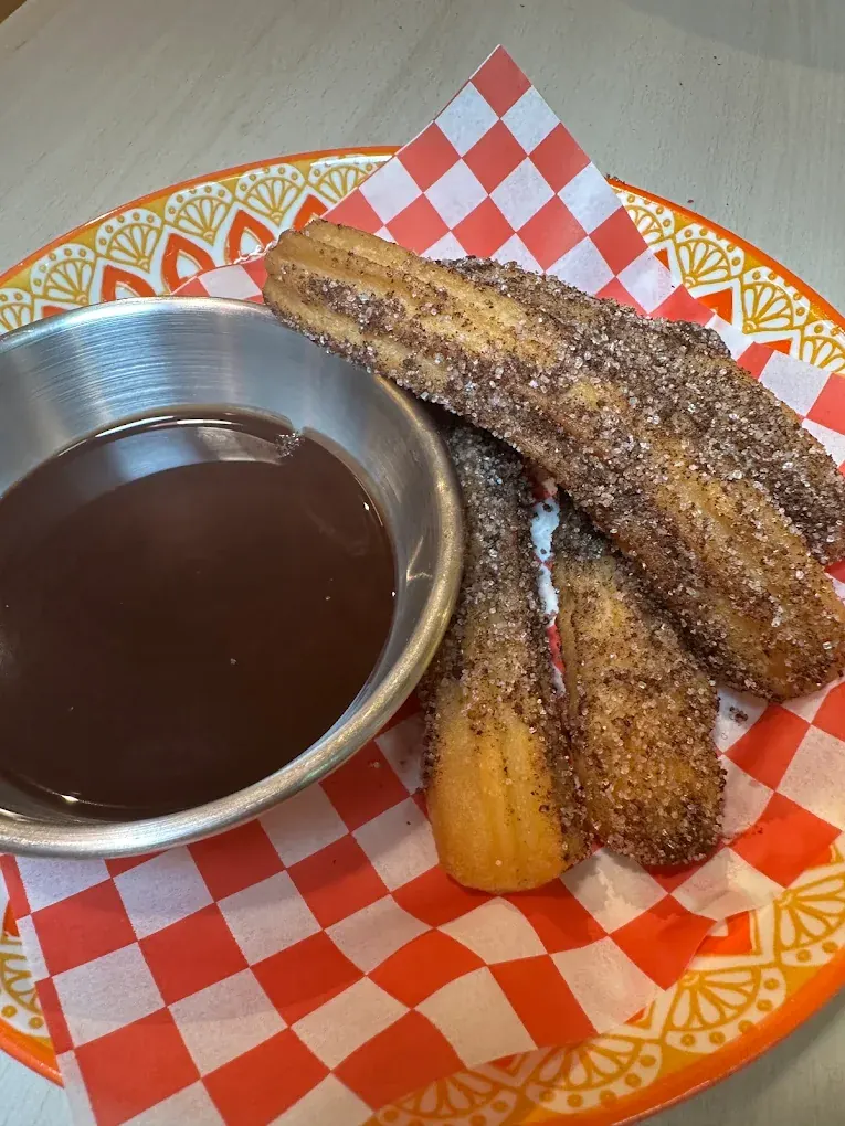 Three cinnamon-sugar churros with a pot of warm chocolate sauce