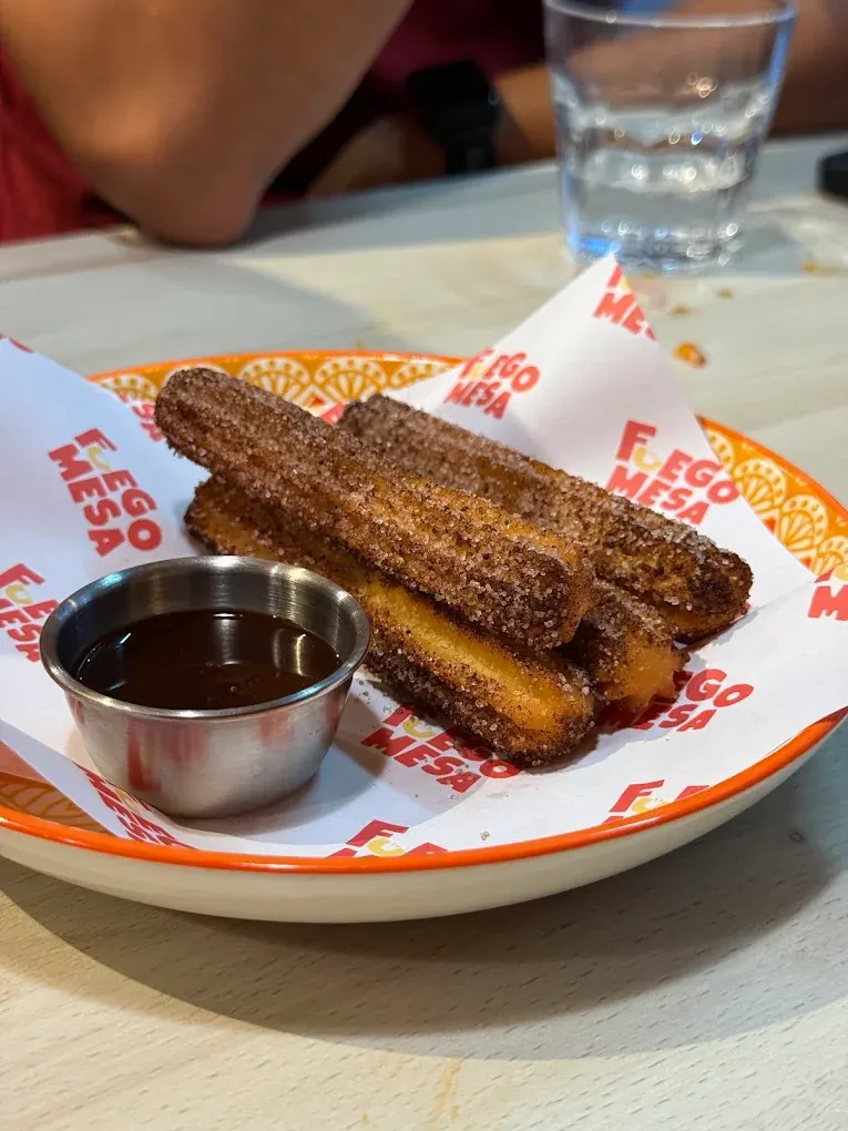 Cinnamon-sugar churros and a pot of chocolate sauce on a branded Fuego Mesa plate
