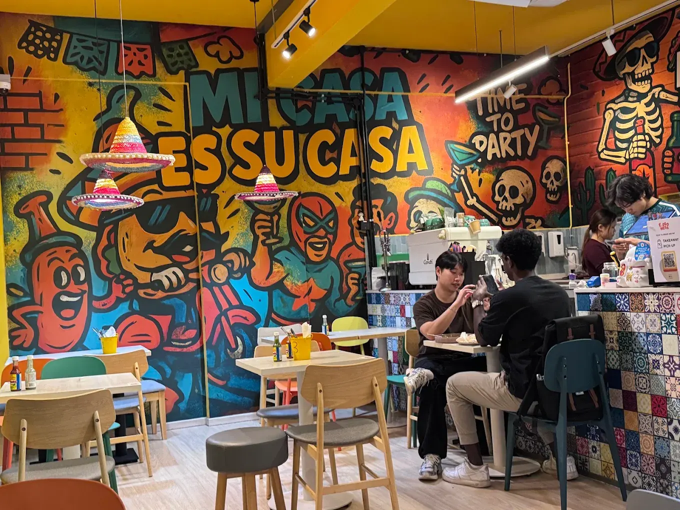 Guests eating beneath the “Mi Casa Es Su Casa” mural and hanging sombrero lampshades