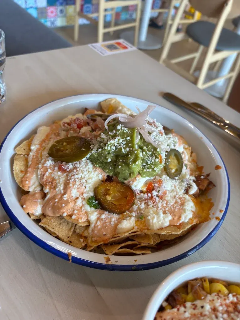 Loaded nachos with jalapeños and guacamole beside a bowl of cheese-topped corn