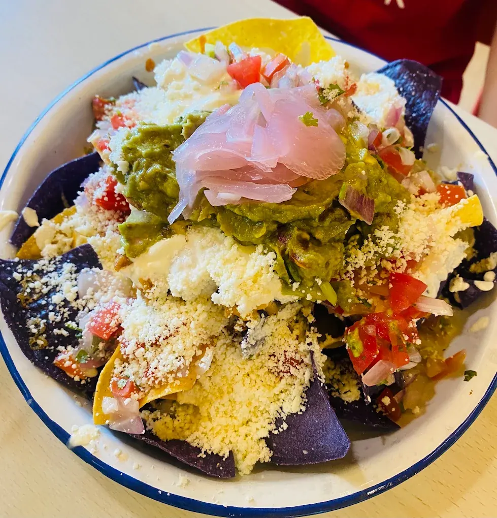 Nachos built on blue and yellow corn chips with guacamole, crumbled cheese and pickled onions