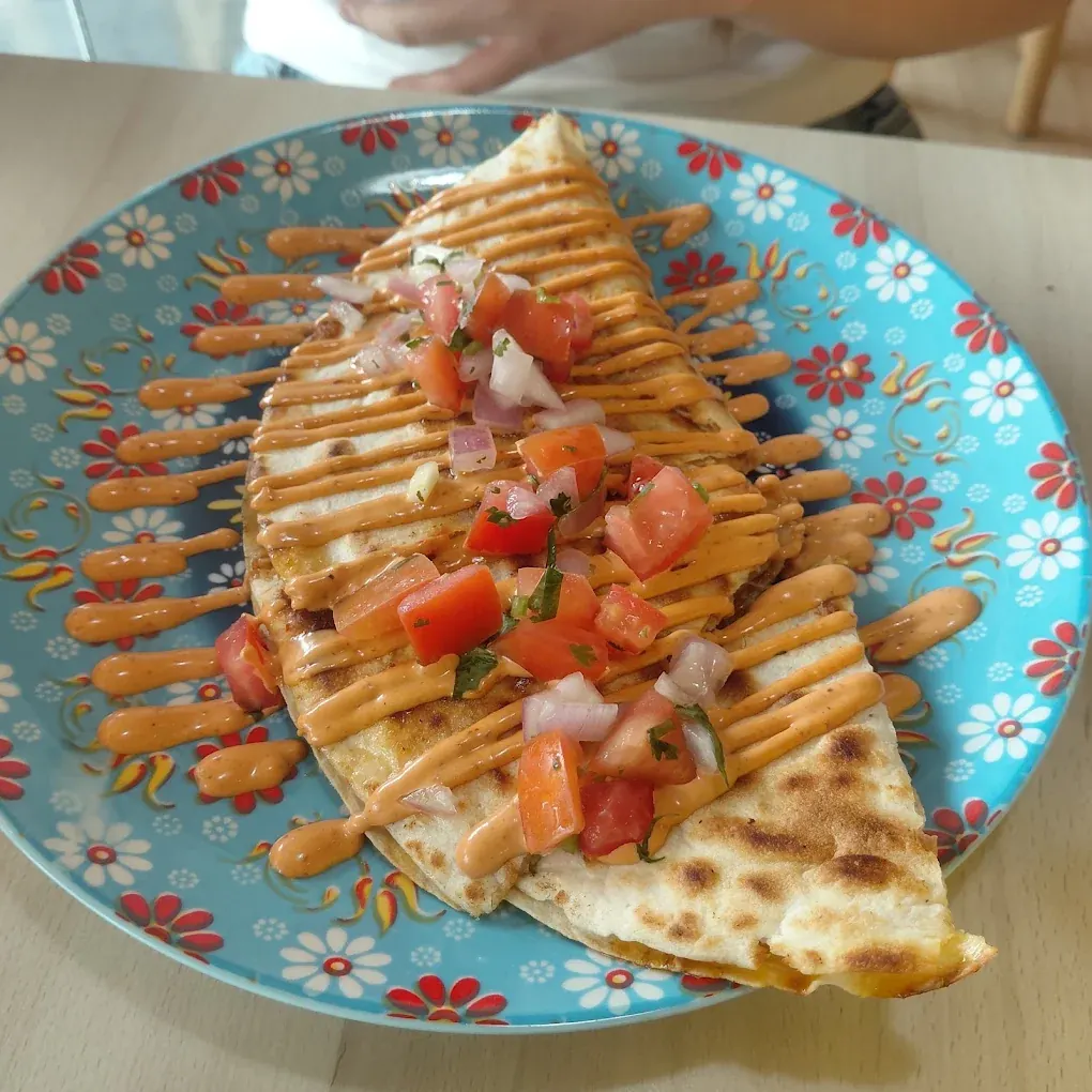 A folded quesadilla on a blue floral plate, striped with chipotle mayonnaise and topped with pico de gallo