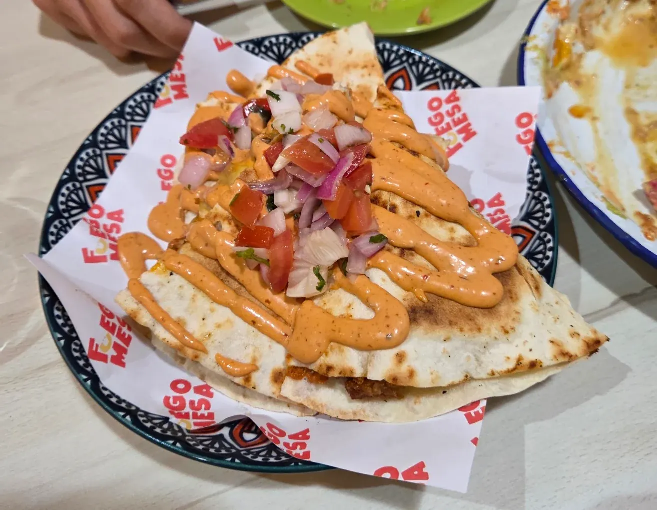 A quesadilla striped with chipotle mayonnaise and topped with fresh pico de gallo on branded Fuego Mesa paper