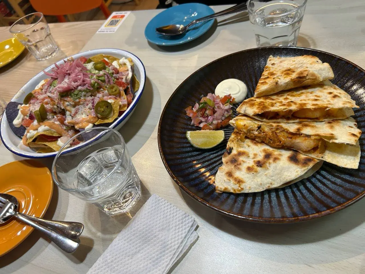 Loaded nachos in an enamel dish beside a plated quesadilla with pico de gallo and lime