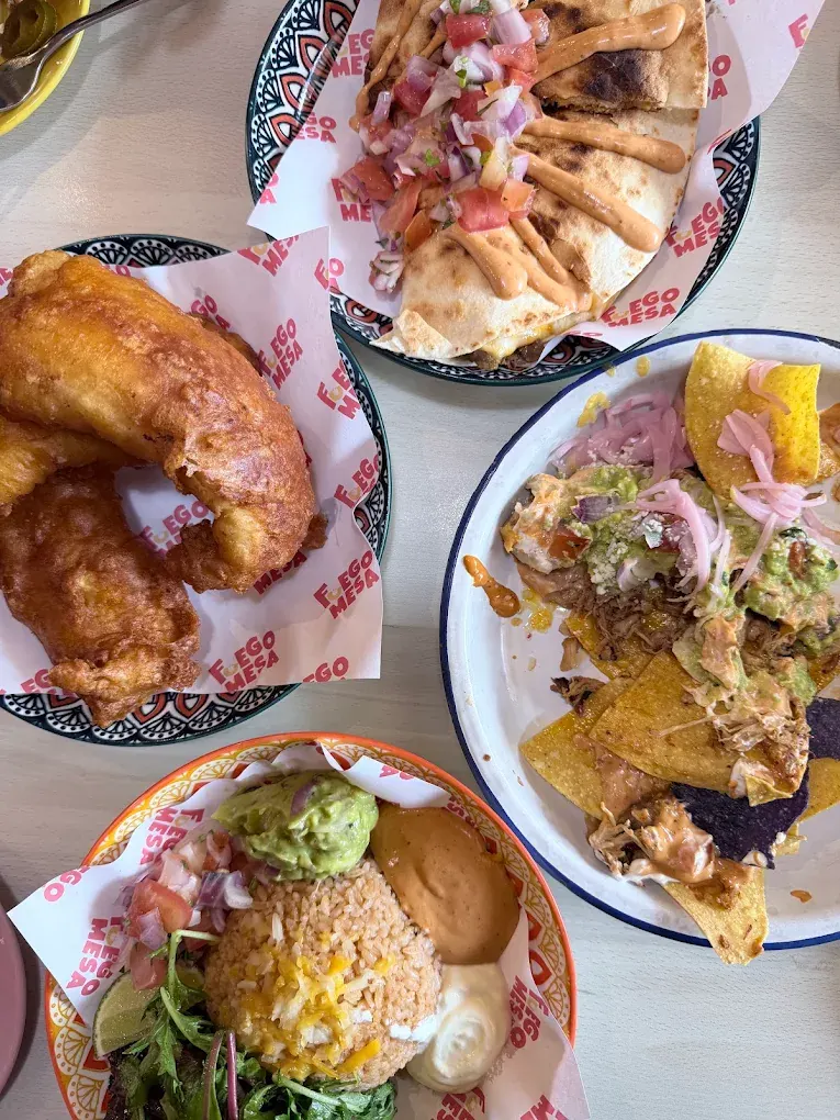 An overhead spread of battered fish, a quesadilla, nachos and a rice plate on Fuego Mesa paper