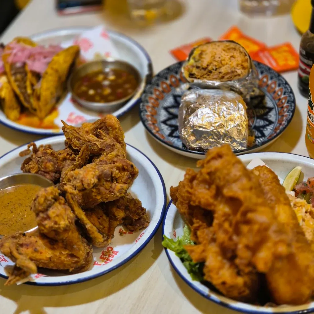 Birria tacos with consommé, a foil-wrapped burrito, fried wings and battered fish shared across a table