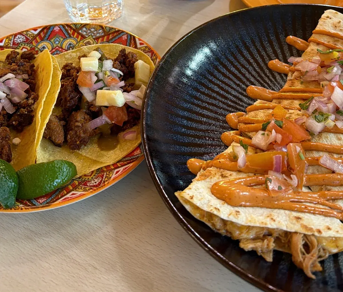 Two tacos with seasoned meat and fruit salsa beside a quesadilla served in a dark bowl