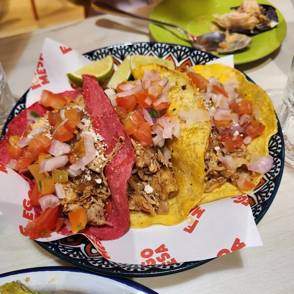 Three tacos on pink and yellow corn tortillas filled with shredded chicken, pico de gallo and crumbled cheese